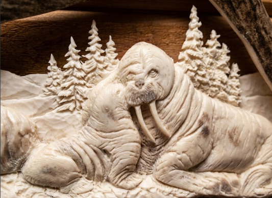 Carved antler  of a walrus momma and baby with a forest background