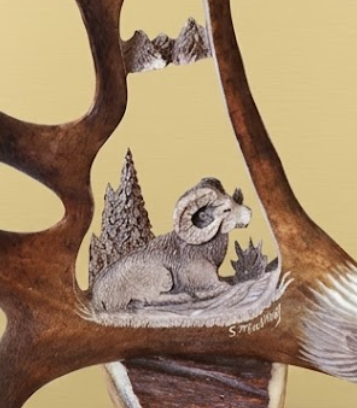 Carved caribou antler with a mountain sheep scene and signature on a beige background