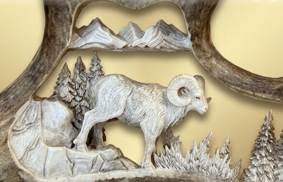 Full curl ram hand carved antler scene with a ram and mountains on a beige background