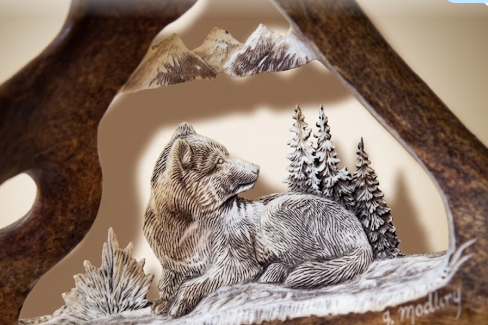 Wolf sculpture in a carved caribou antler framed with mountain and tree background