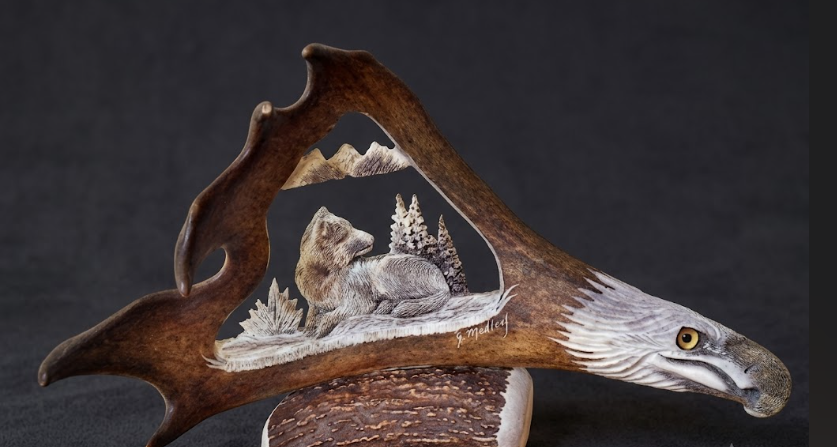 Antler sculpture of a wolf  in a natural setting with mountains and trees.