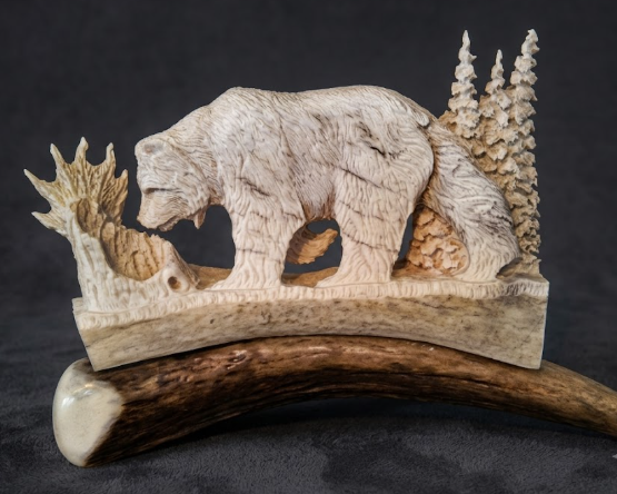 Antler carving of a bear and trees on a dark background