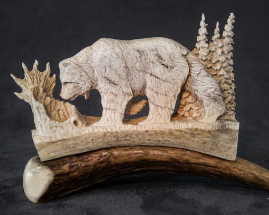 Antler carving of a bear and trees on a dark background