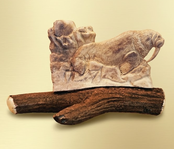 Carved antler  figure of a bull walrus on a rock  on a beige background