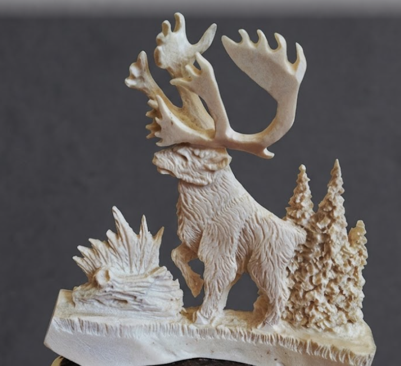 Carved caribou figure with antlers on a base with trees and rocks against a dark background