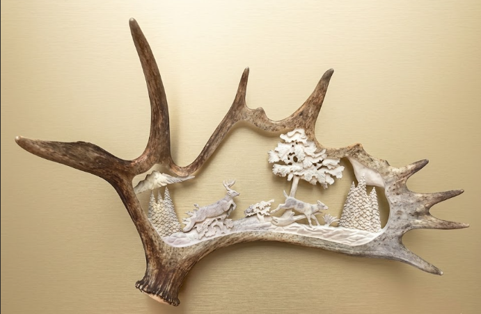 Decorative wall art made from a moose antler with a scene of deer and trees on a beige background