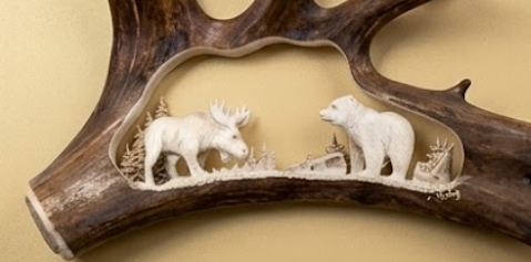 Carved antler with moose and bear figures on a beige background