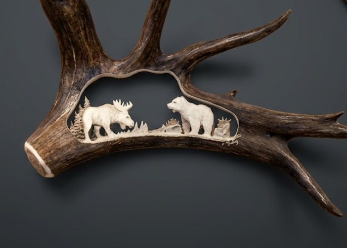 Carved deer antler with white bear and moose figures on a dark background