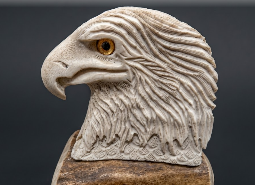 Carved stone eagle head on a wooden base against a dark background