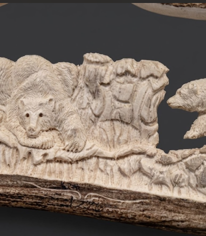 Carved ivory piece with bear and landscape design on a dark background