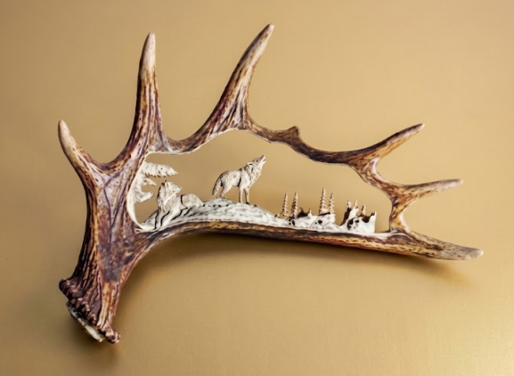 Decorative antler with carvings of a wolf and landscape on a beige background