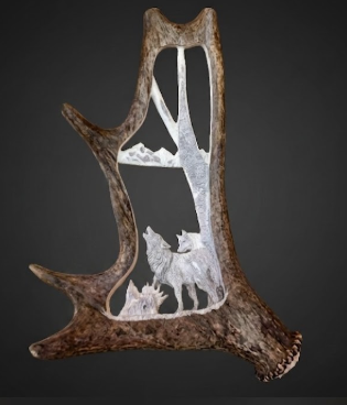 Decorative antler with cut-out design of wolves and mountains on a dark background