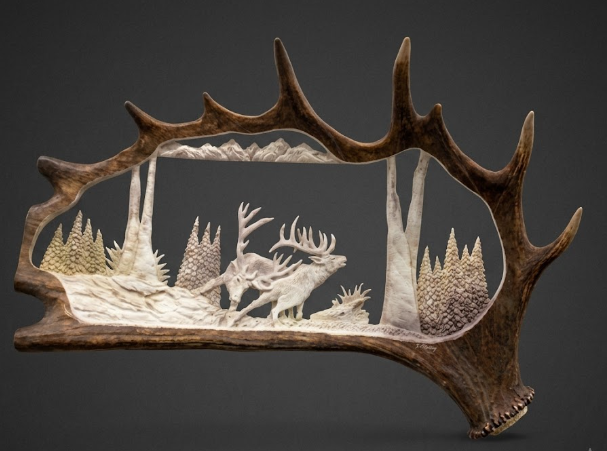 Carved deer antler with a detailed landscape of deer and trees inside