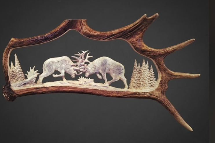 Decorative antler with carvings of two deer and trees on a dark background