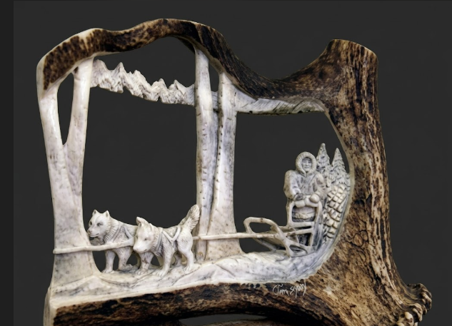 Antler carved wooden scene with a person, dog, and landscape on a dark background