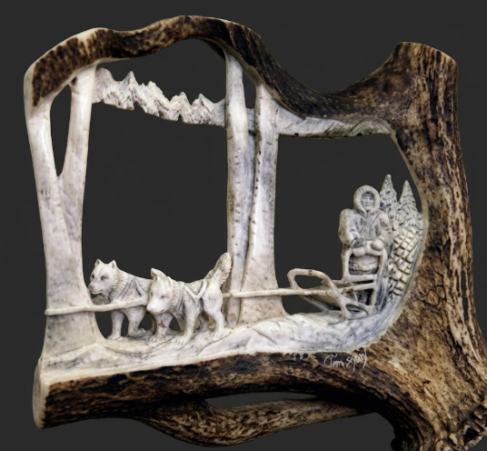 Caribou antler carving of a sled and dogs, on a dark background