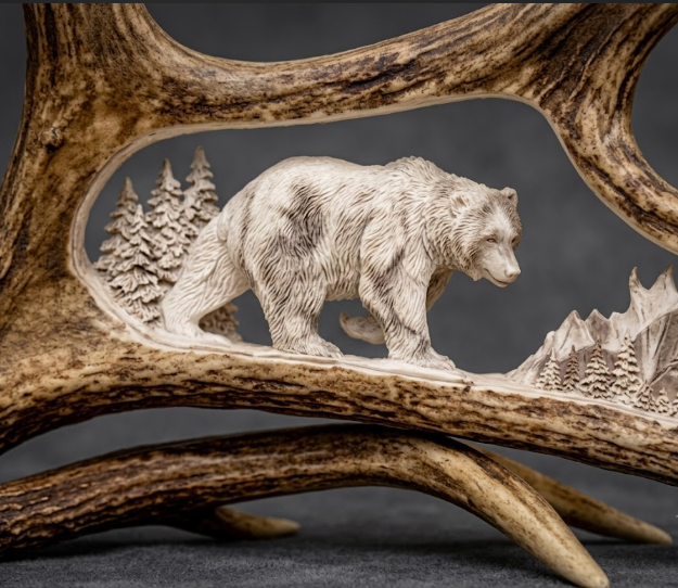 Carved bear on a moose antler with forest scene