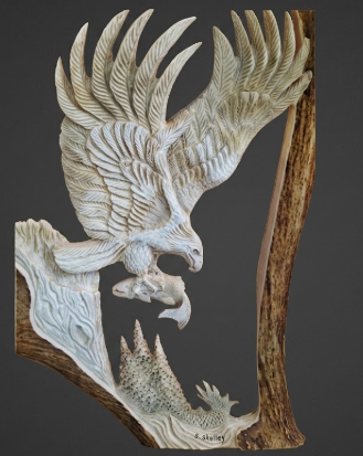 Carved moose antler sculpture of an eagle with outstretched wings getting its dinner on a dark background
