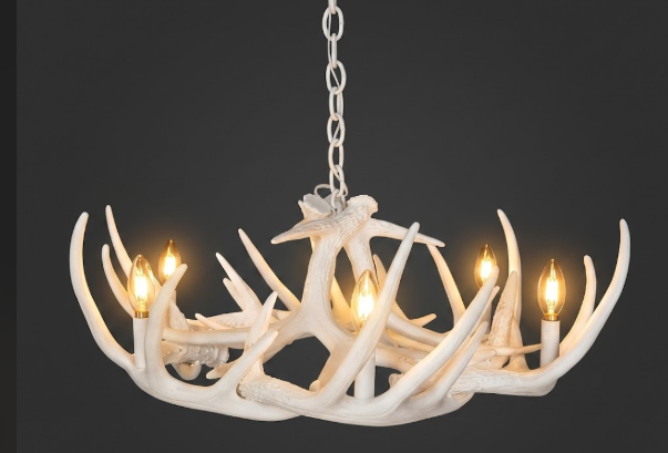 faux deer White antler chandelier with four lit lights on a dark background