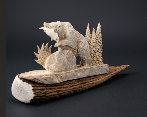 Carved stone sculpture of a bear with fish on a rock, set against a dark background