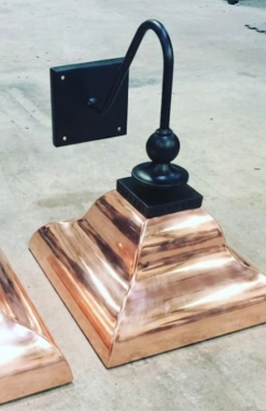 Copper wall sconce and black metal decorative post cap on a concrete surface