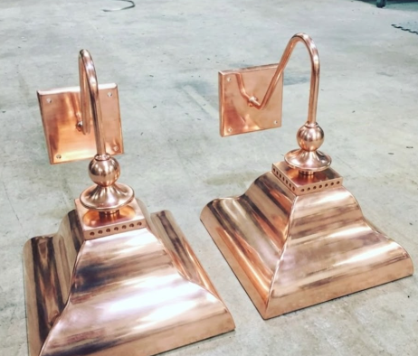 Two copper wall sconces finials on a concrete floor