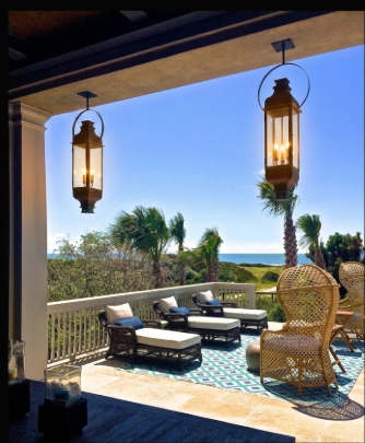 Two copper pendant lights or lanterns hanging from a ceiling on a sunny day, with outdoor furniture and a pool in the background.