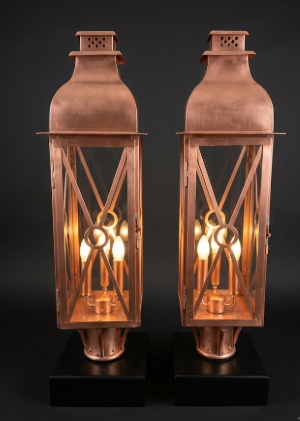 Two copper foyer lanterns with lit candles on a black background