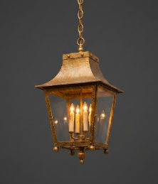 Gold Decorative outdoor pendant foyer light hanging against a stone wall lantern with glass panels on a dark background