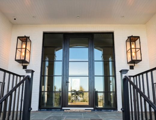 Black glass front entryway door with wall lights on a white house exterior
