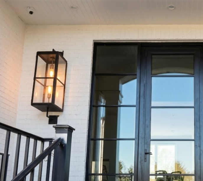 Decorative  entryway light fixture on a white brick wall next to a glass door.