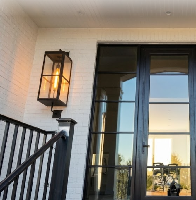 Outdoor entryway light fixture on a white brick wall next to a glass door.