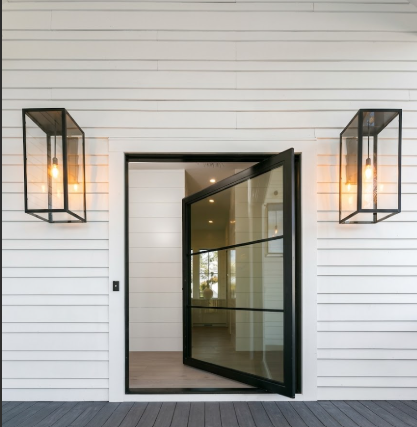 Modern glass door with black frame and entryway wall lights on a white wooden house exterior.