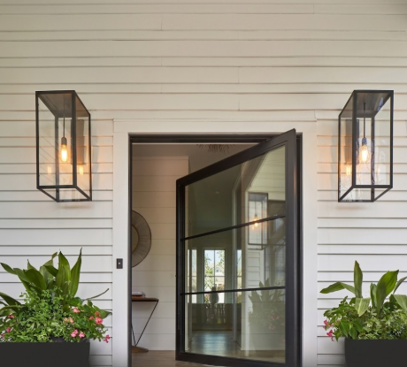 Modern front door with black frame and glass panels, flanked by two black glass foyer entryway lights on a white wood wall near a glass door.