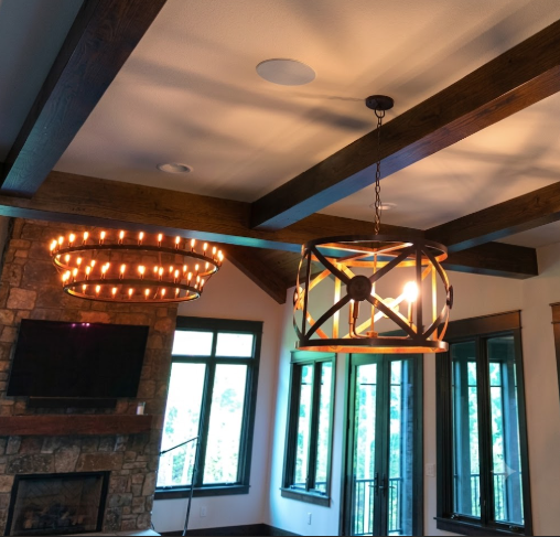 Living room with wooden beams, a 2 tier foyer entryway pendant light chandelier hanging from a wooden ceiling and large windows.