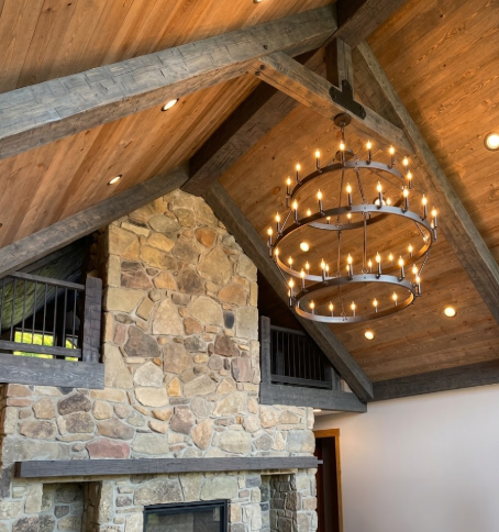  3 tier foyer entryway pendant light chandelier hanging from a wooden ceiling with stone wall and fireplace in the background