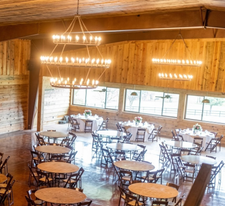 Large room with  3 tier foyer entryway pendant light chandelier wooden walls and ceiling, tables, and chairs set up for an event.