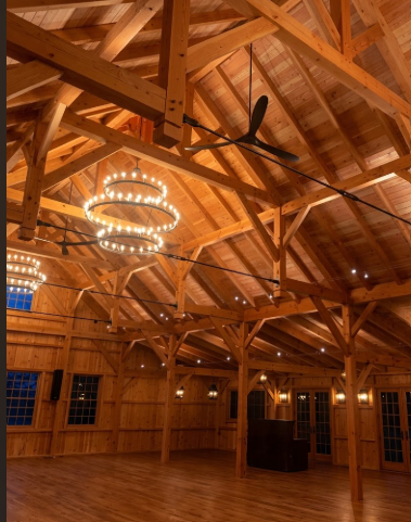 Wooden interior of a large room with high ceiling and  3 tier foyer entryway pendant light chandelier hanging from a wood ceiling.