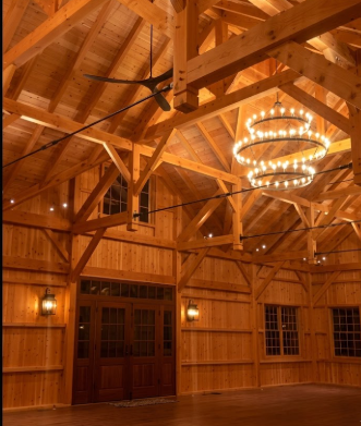 Wooden interior of a large room with high ceiling and  3 tier foyer entryway pendant light chandelier hanging from a wood ceiling.