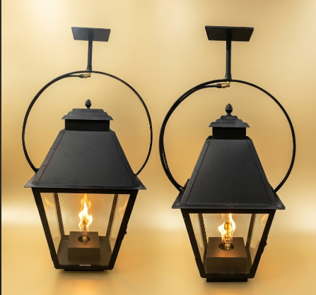 Two black outdoor foyer entryway pendant lights with a warm glow on a beige background