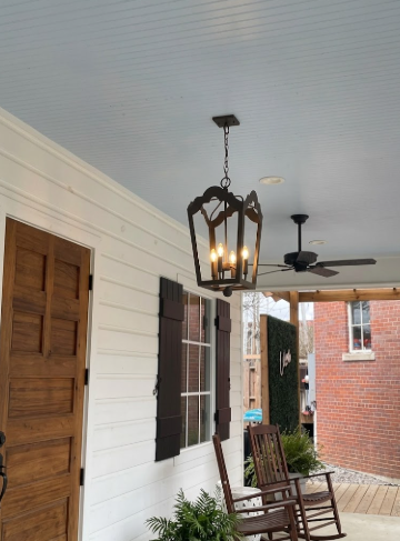 Front porch with wooden door, rocking chairs, and decorative lantern on a white house.