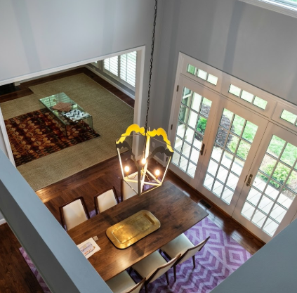 Aerial view of a dining room with a pendant light, wooden table and chairs, a rug, and a large window.