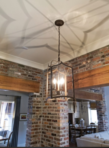 A kitchen island pendant light or chandelier hanging from a coffered ceiling in a room with brick walls and a dining table