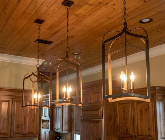 Three hanging kitchen island pendant light or chandelier light fixtures in a room with wooden ceiling and cabinets.