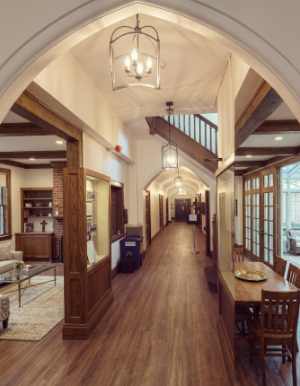 Long hallway with 4 kitchen island pendant lights or chandeliers and a wooden floors and arches, featuring a staircase and various rooms.