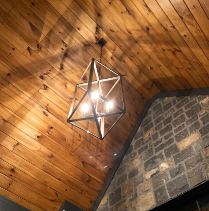 Geometric chandelier hanging from a wooden ceiling with stone wall background