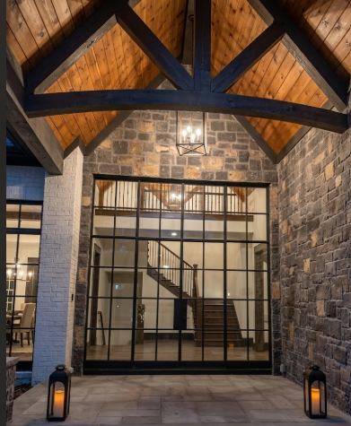 A modern interior with entryway pendant light, stone walls, wooden beams, and a glass door leading to another room.