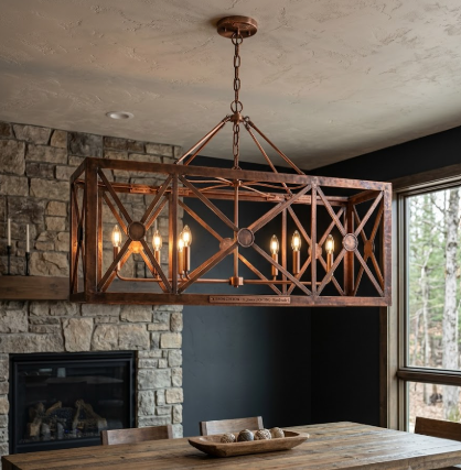 Copper chandelier hanging above a dining table with a stone wall and fireplace in the background.