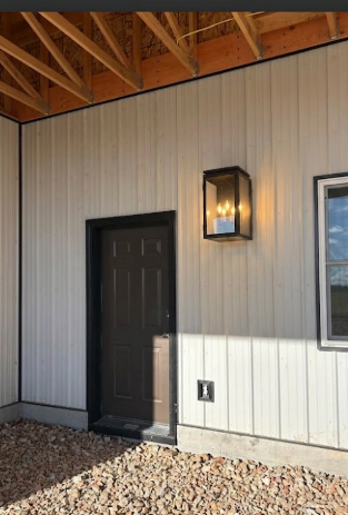 Modern exterior wall with a door, light fixture, and pebbled ground.