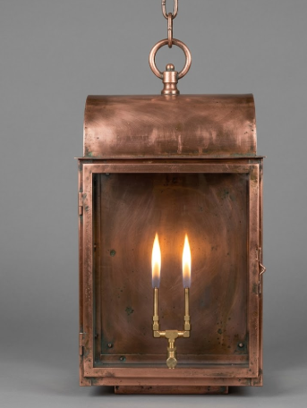 Copper pendant light lantern with two lit candles inside on a gray background